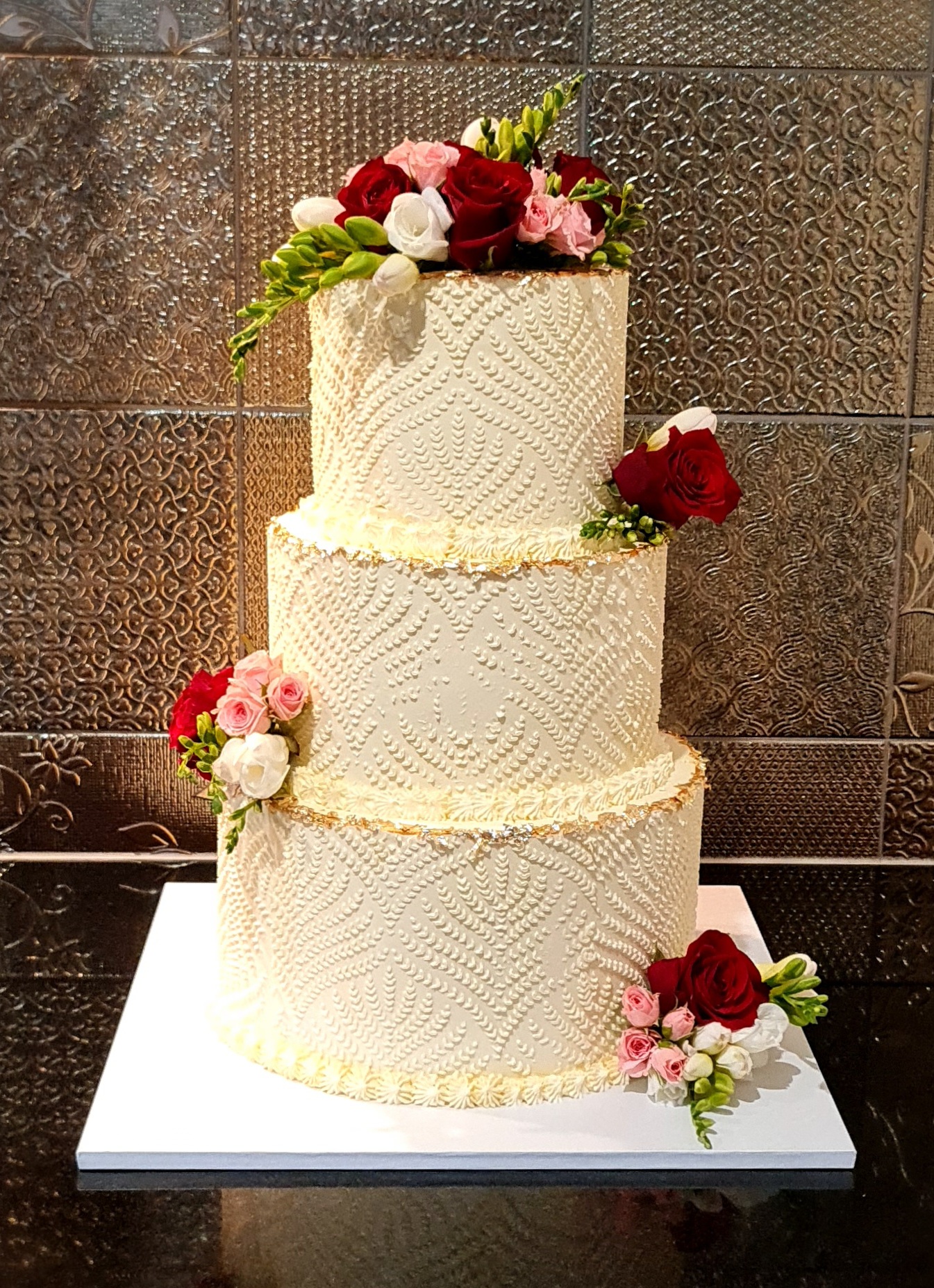 Elegant three-tier white wedding cake with intricate piping and fresh roses